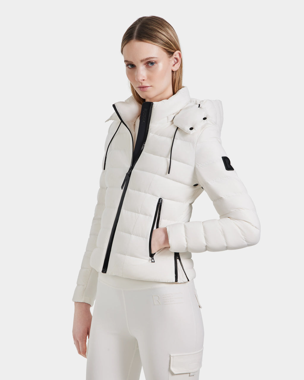 A woman with straight blonde hair models the Rudsak MELISSA - 8124031 Cotton White lightweight down puffer jacket with black zippers and matching white pants, posed against a plain white background.