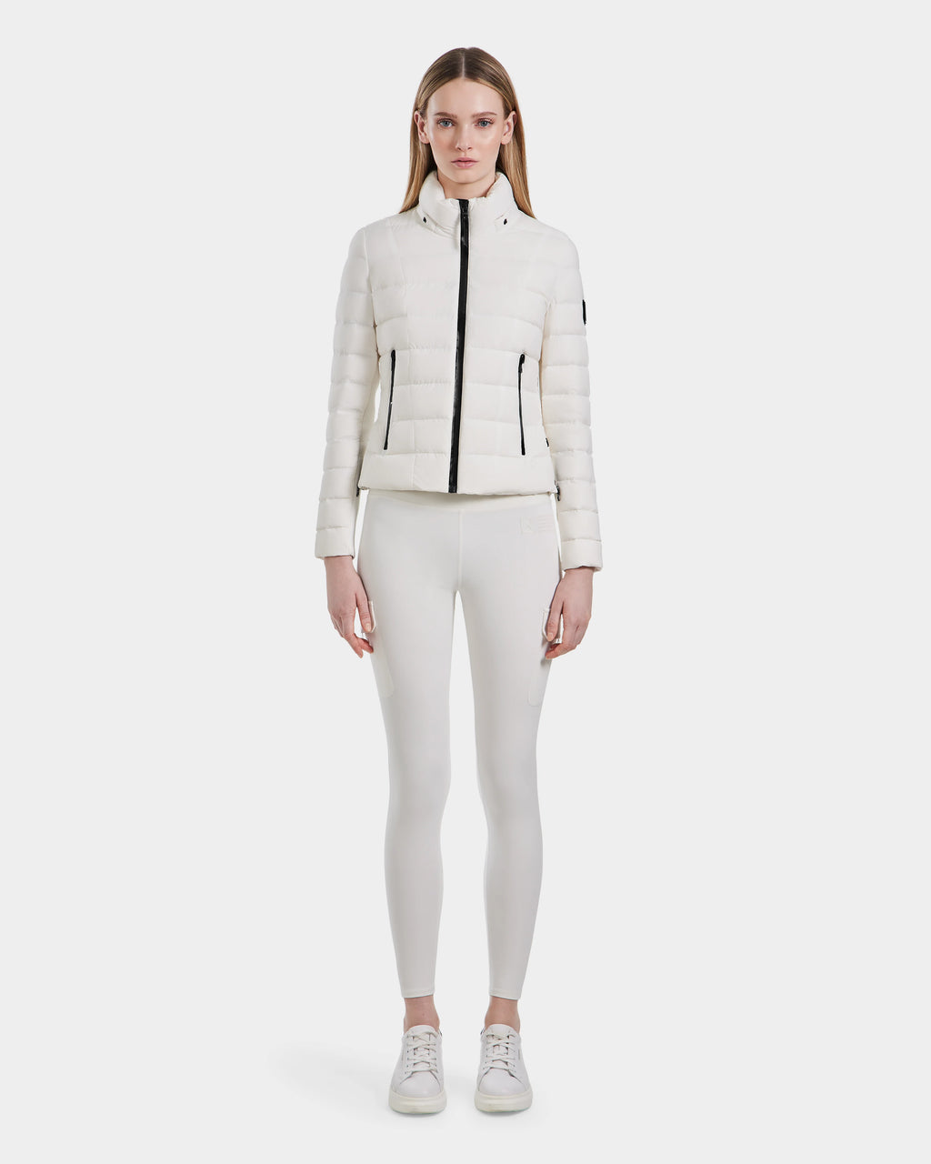 A woman faces forward wearing the Rudsak MELISSA - 8124031 Cotton White lightweight down puffer jacket, styled with white leggings and sneakers against a plain light background.
