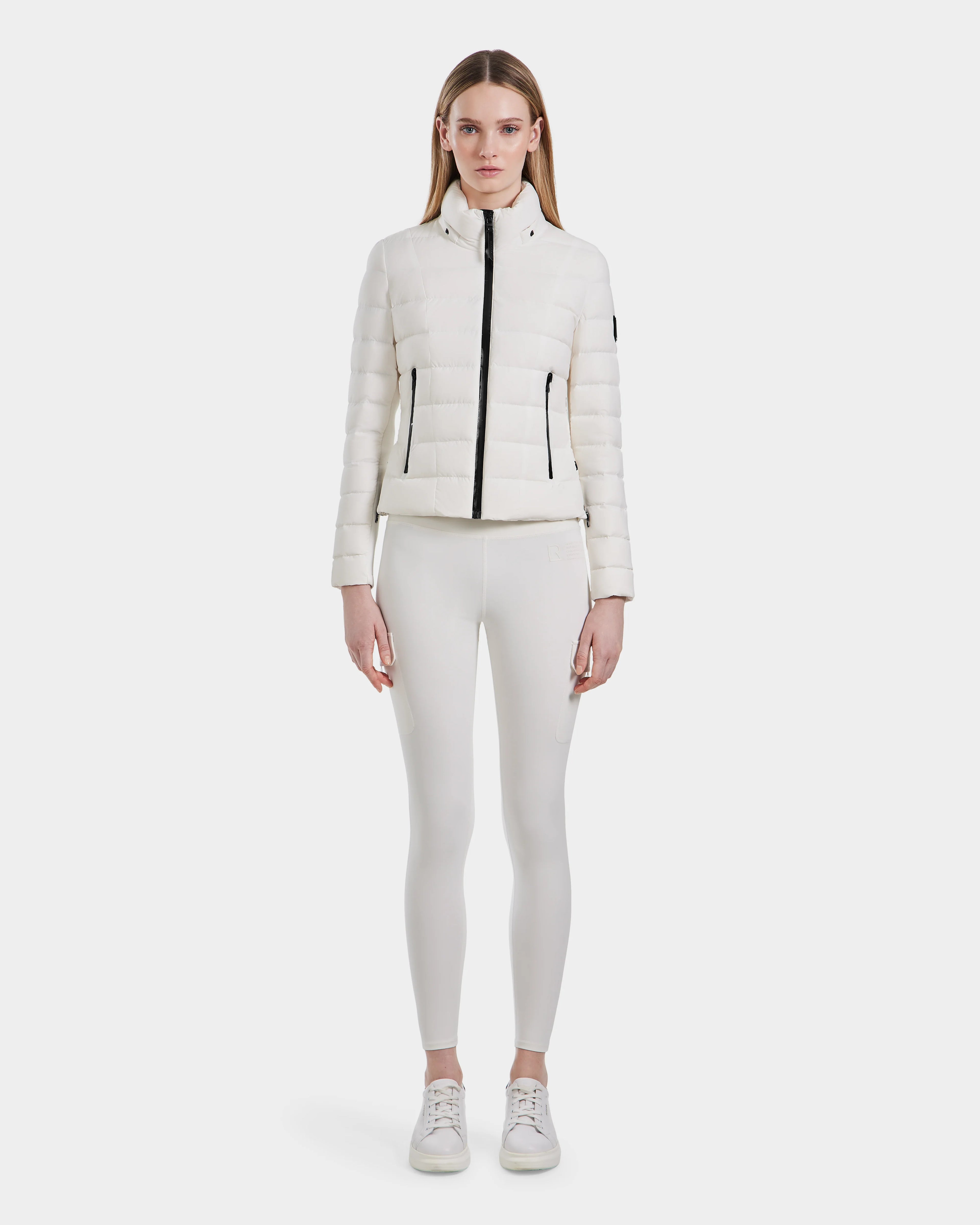 A woman faces forward wearing the Rudsak MELISSA - 8124031 Cotton White lightweight down puffer jacket, styled with white leggings and sneakers against a plain light background.