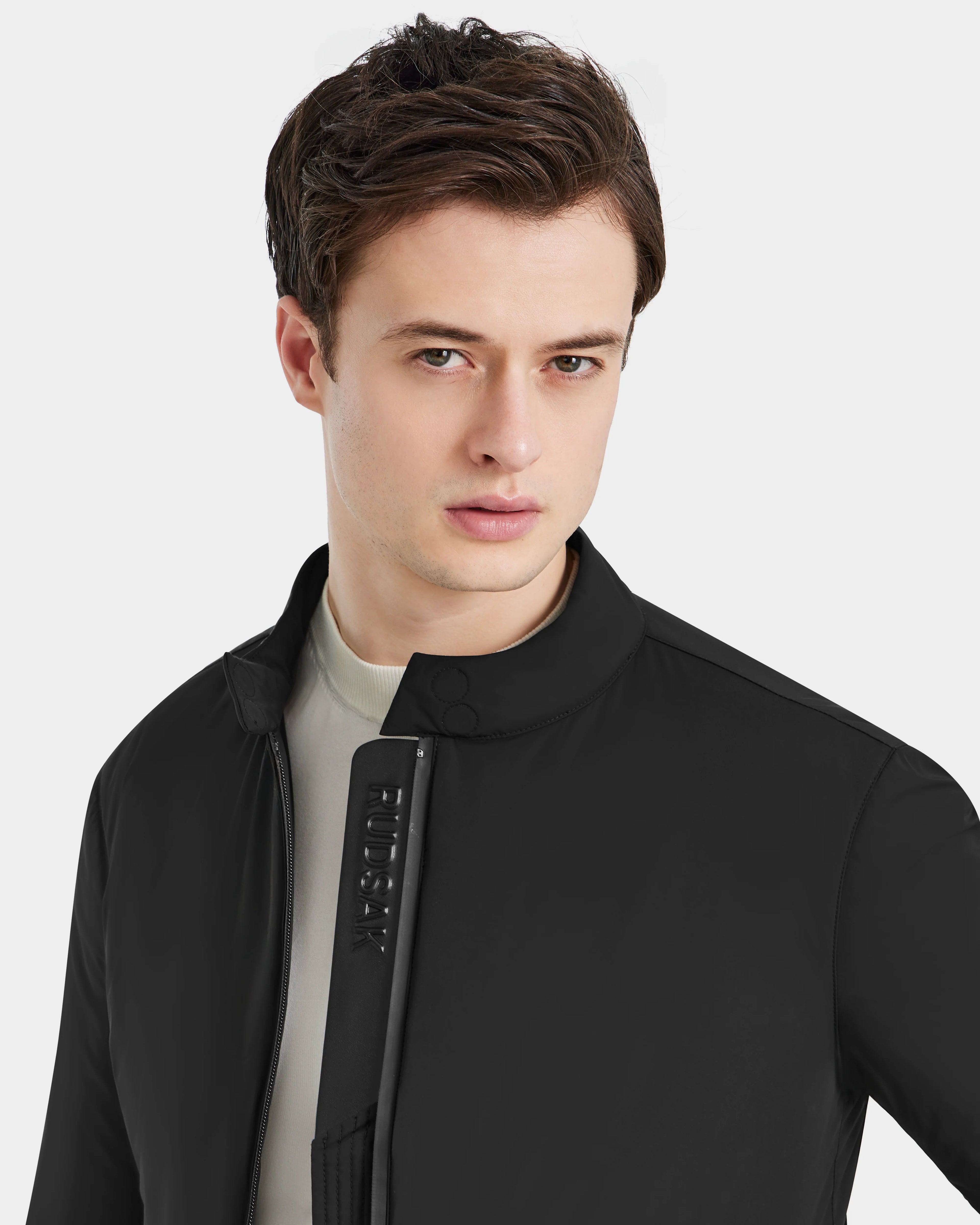 A young man with short brown hair wears the Rudsak PETER - 6125001 Black lightweight bomber jacket over a light shirt, looking directly at the camera with a neutral expression against a plain light background.