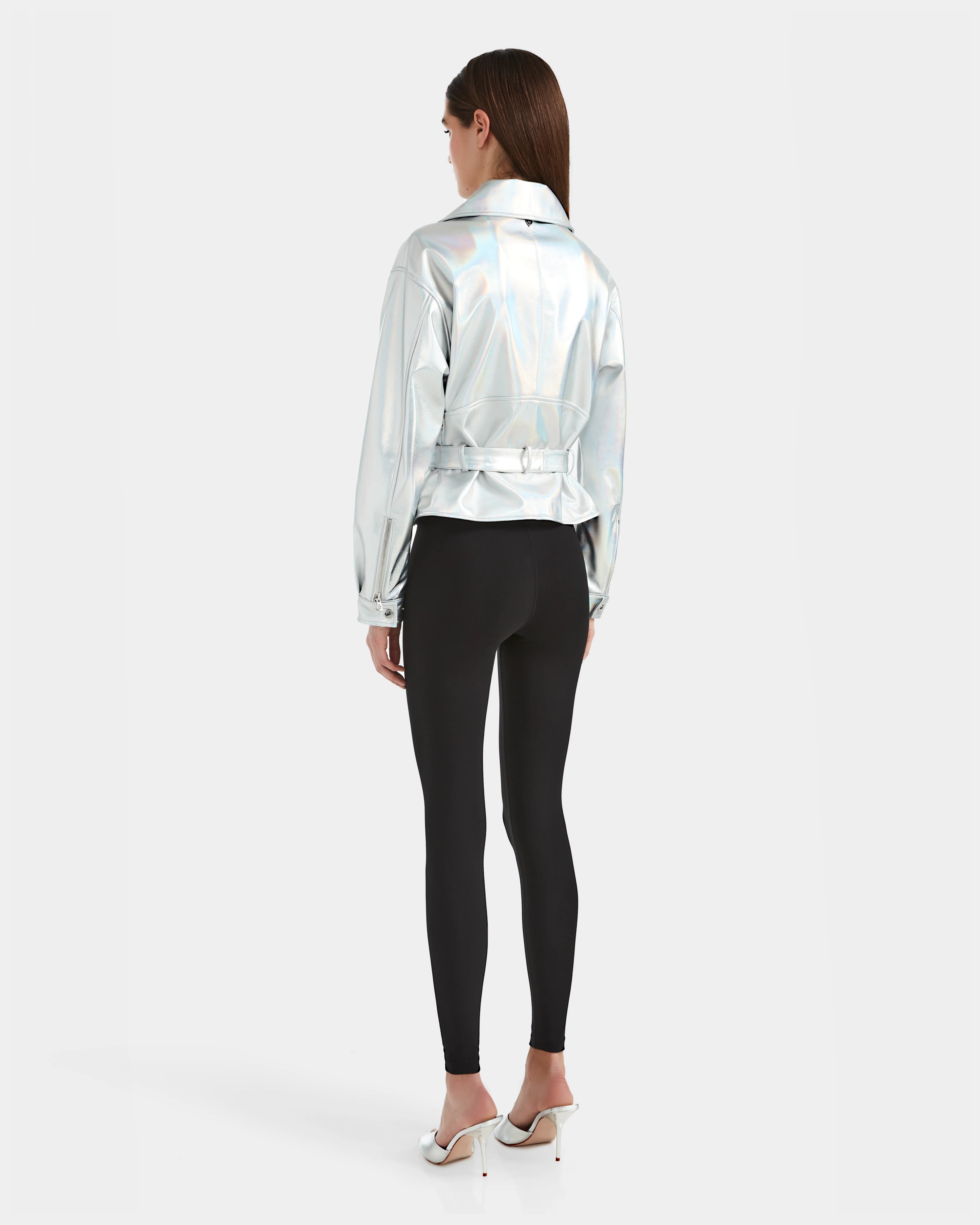 A woman faces away, wearing the Rudsak ARIELLE - 8124052 Iridescent Cotton White jacket, black leggings, and white high heels against a plain white background.
